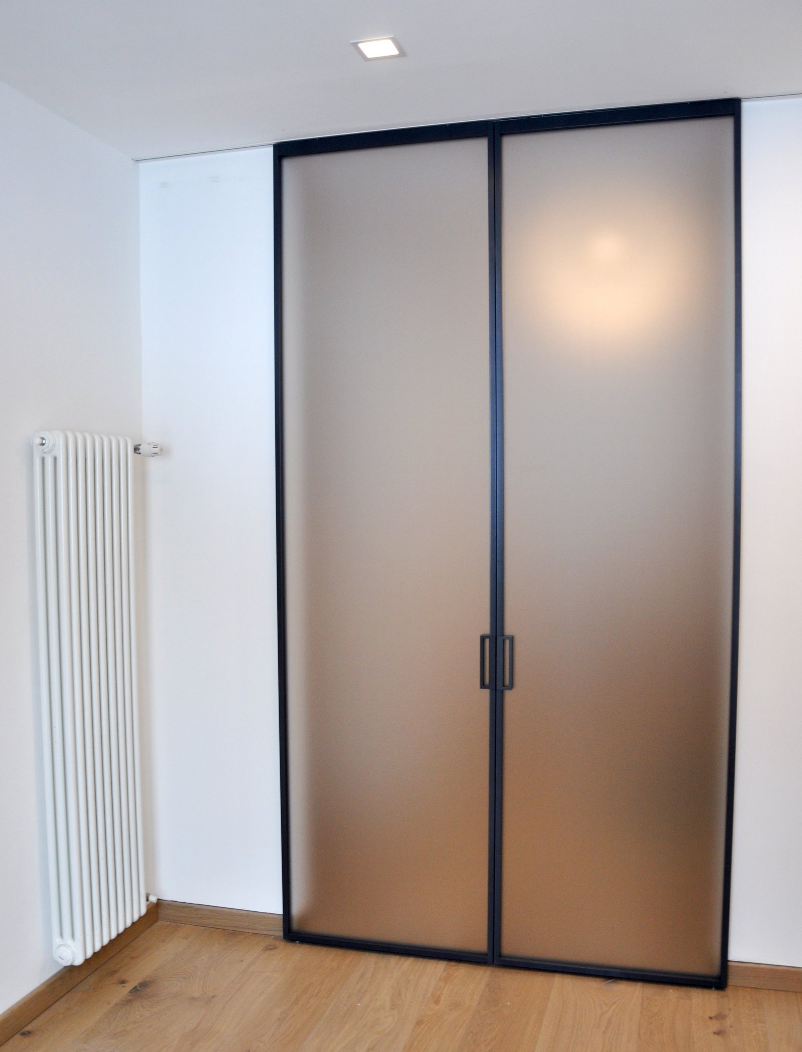 Porta doppia scorrevole con telaio minimal in alluminio nero e grandi vetrate satinate color bronzo per interni.